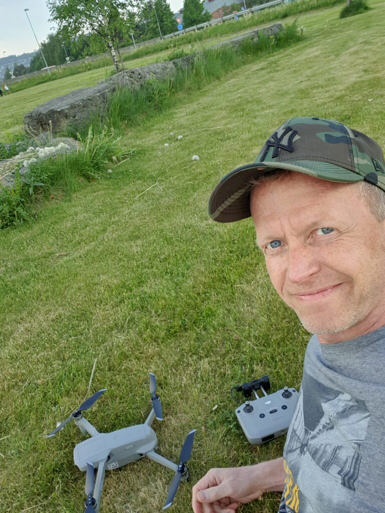 Frode Friestad, redaktør i Droneavisa, sitter i gresset med en DJI Air 2 og kontrolleren foran seg, sommeren 2021