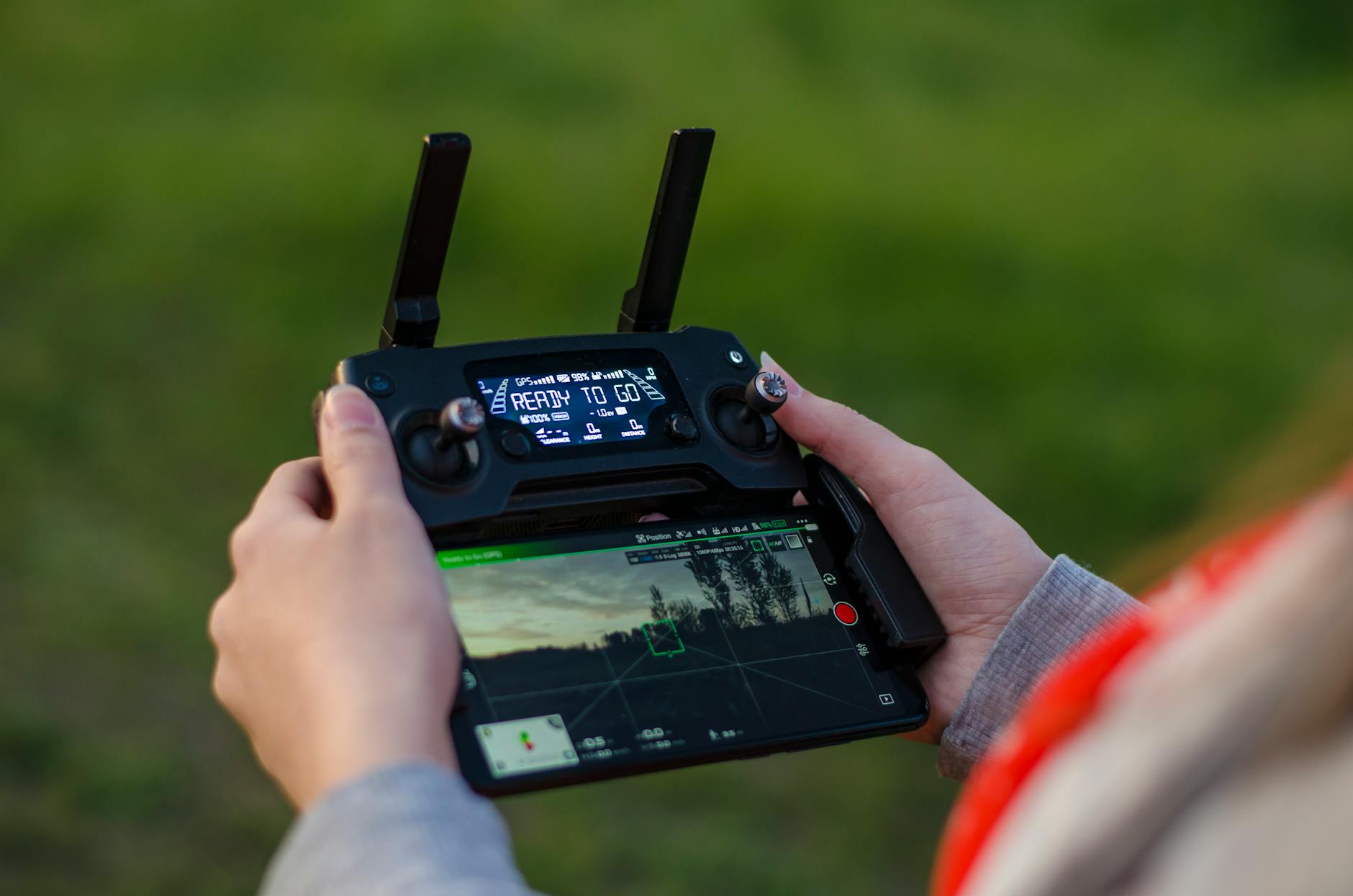 Close-up of hands holding a DJI drone controller outdoors with green background.
