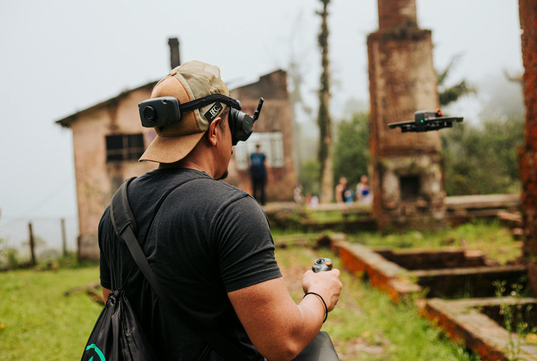 A man uses a drone in a misty, abandoned building site surrounded by greenery.
