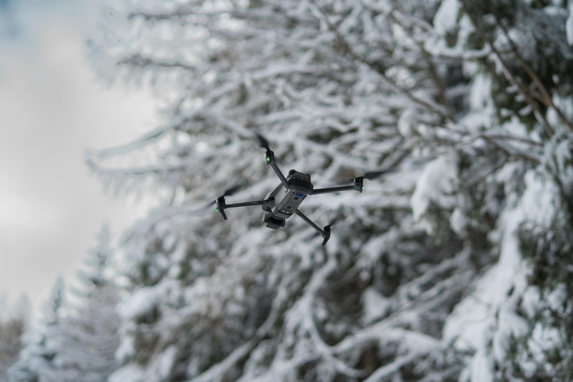 A drone soars through a wintery forest in Trento, Italy, against a blurred snowy background.