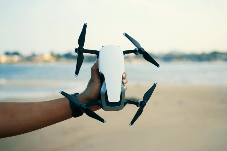 Fiber-optisk FPV-drone med synlig kabelspole flyr lavt over åpent landskap nær trerekke.