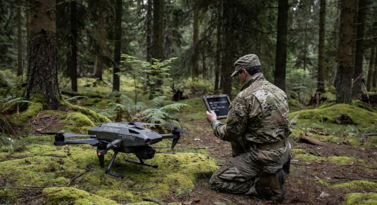 Soldat i feltuniform opererer liten quadkopter-drone under militærøvelse i skogsterreng.