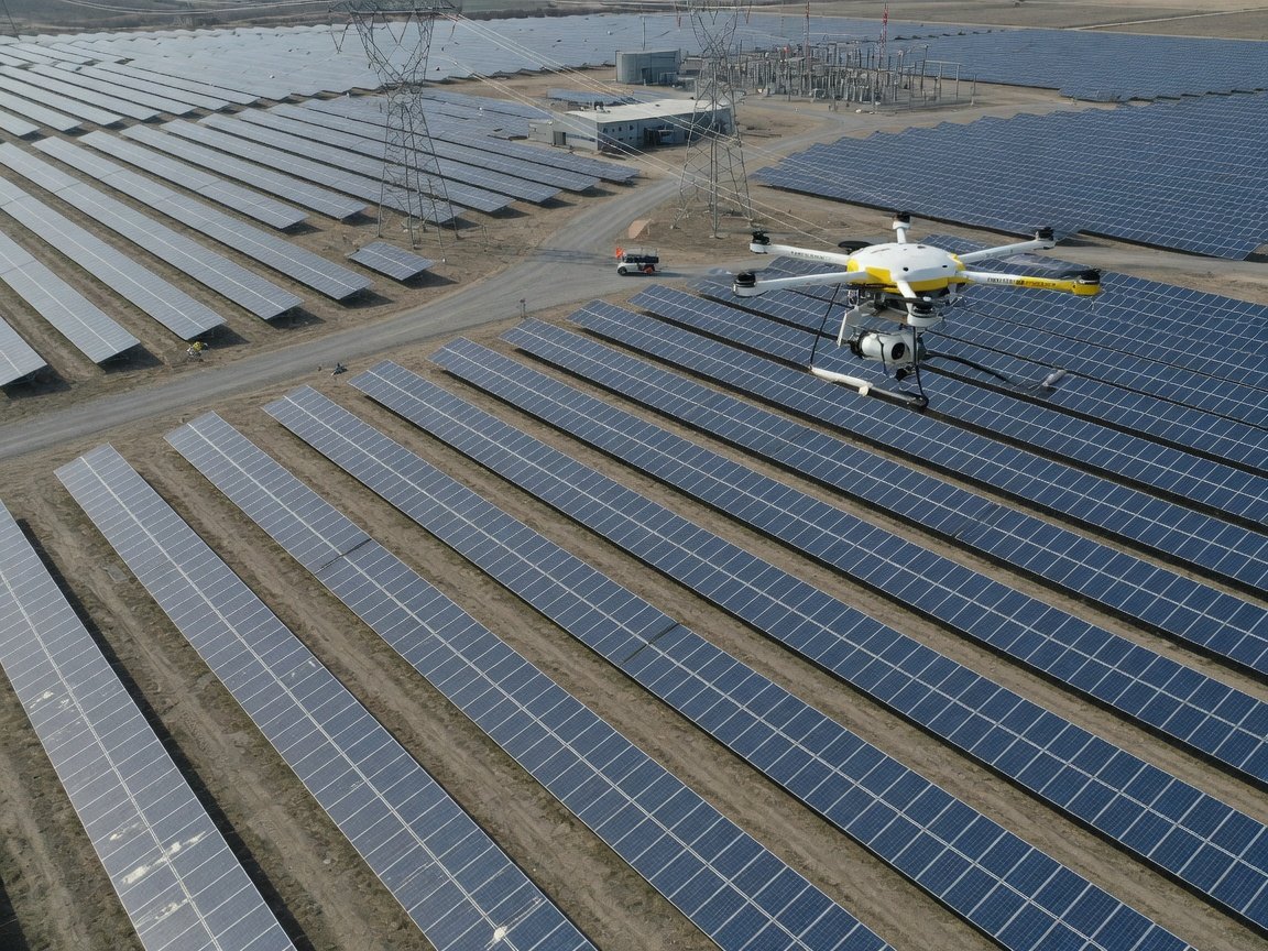Inspeksjonsdrone over solpanelanlegg med rader av solcellepaneler synlig under.