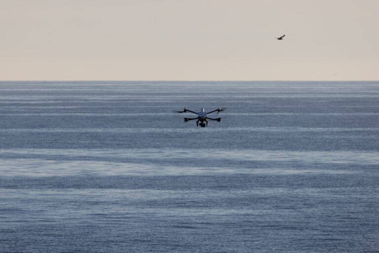 Termisk drone for nødetater i luften over skoglandskap, med kartleggingsutstyr synlig under dronen.