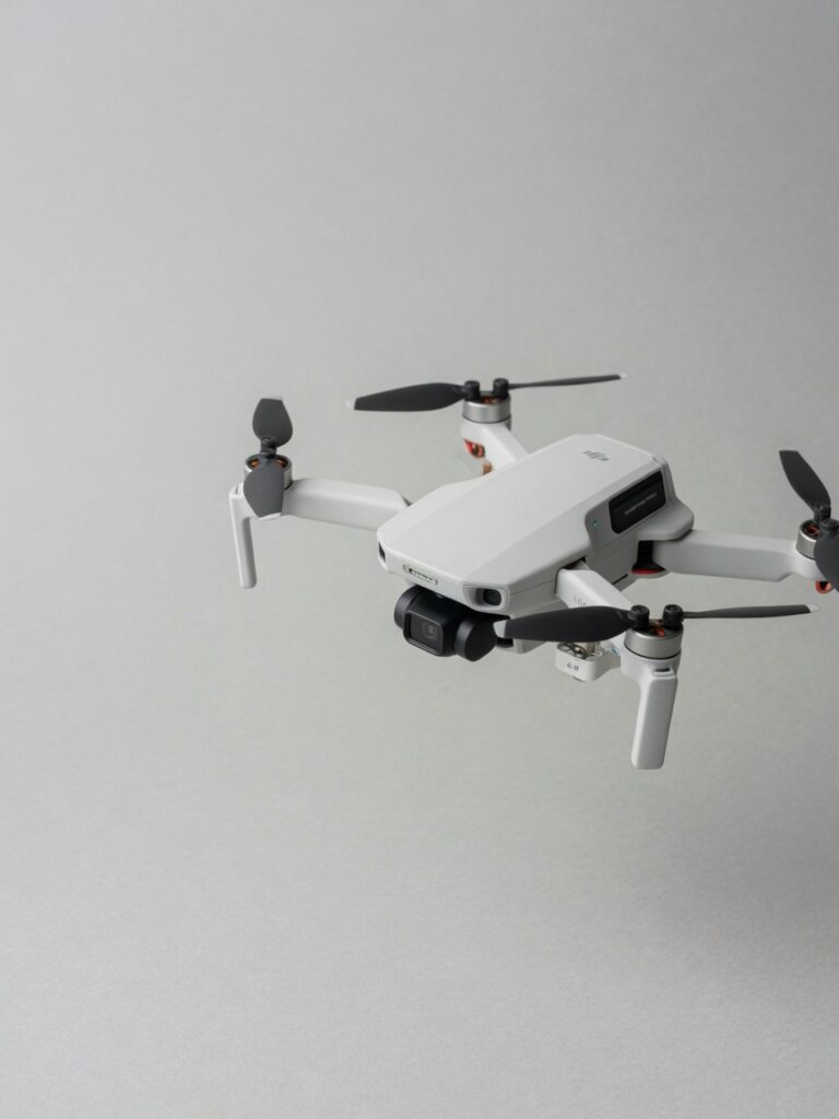 Liten hvit DJI-drone i luften med propellene i bevegelse mot nøytral bakgrunn.