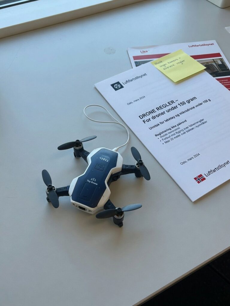 Liten leketøysdrone uten kamera på nøytral bakgrunn, ved siden av amerikansk regelverksdokument.