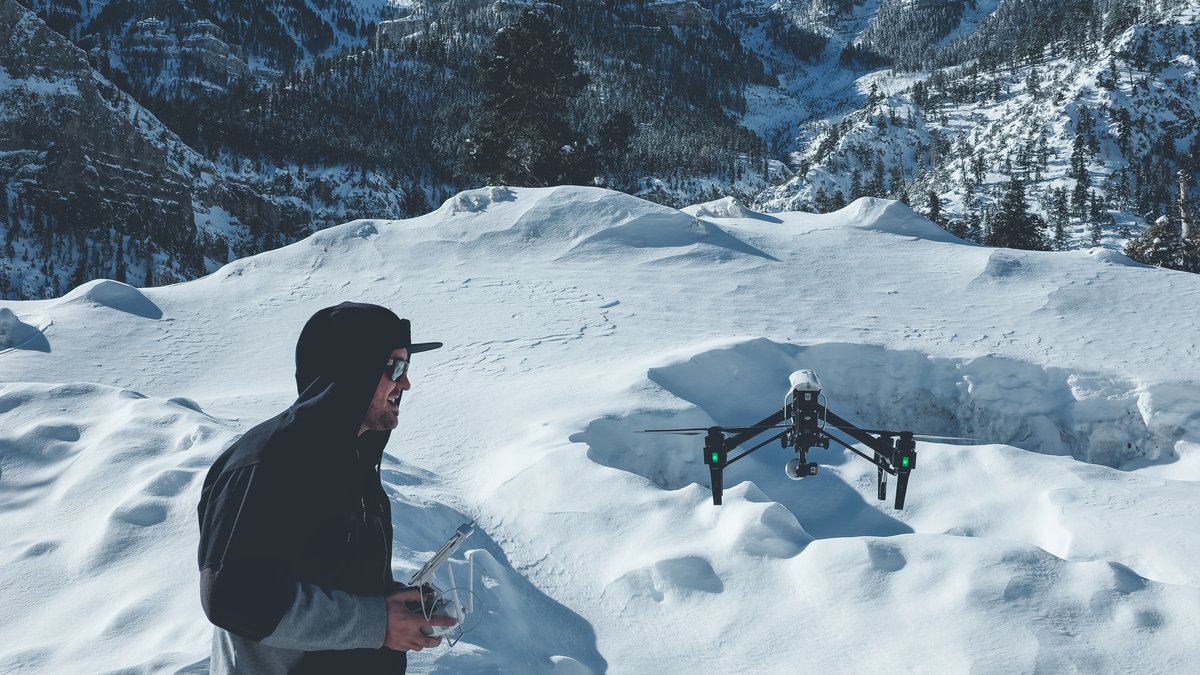 Dronepilot styrer drone lavt over snødekt fjellandskap i vinterforhold