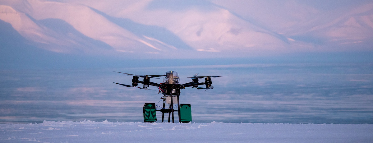Liten drone som flyr over snødekt arktisk landskap med fjell i bakgrunnen under kaldt lys