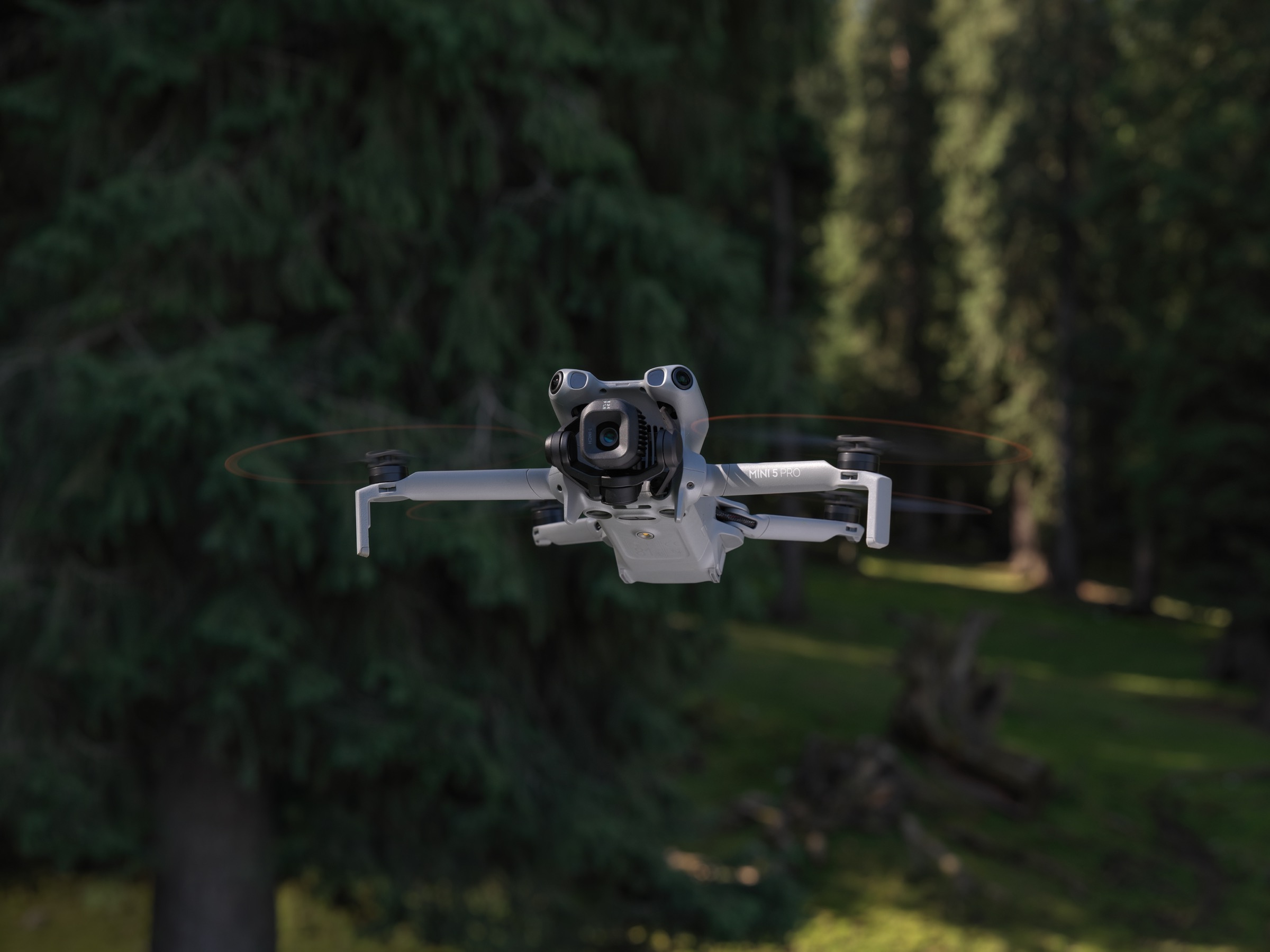 Liten sammenleggbar kameradrone med front-LiDAR svever lavt over en gresslette i sommerlys.