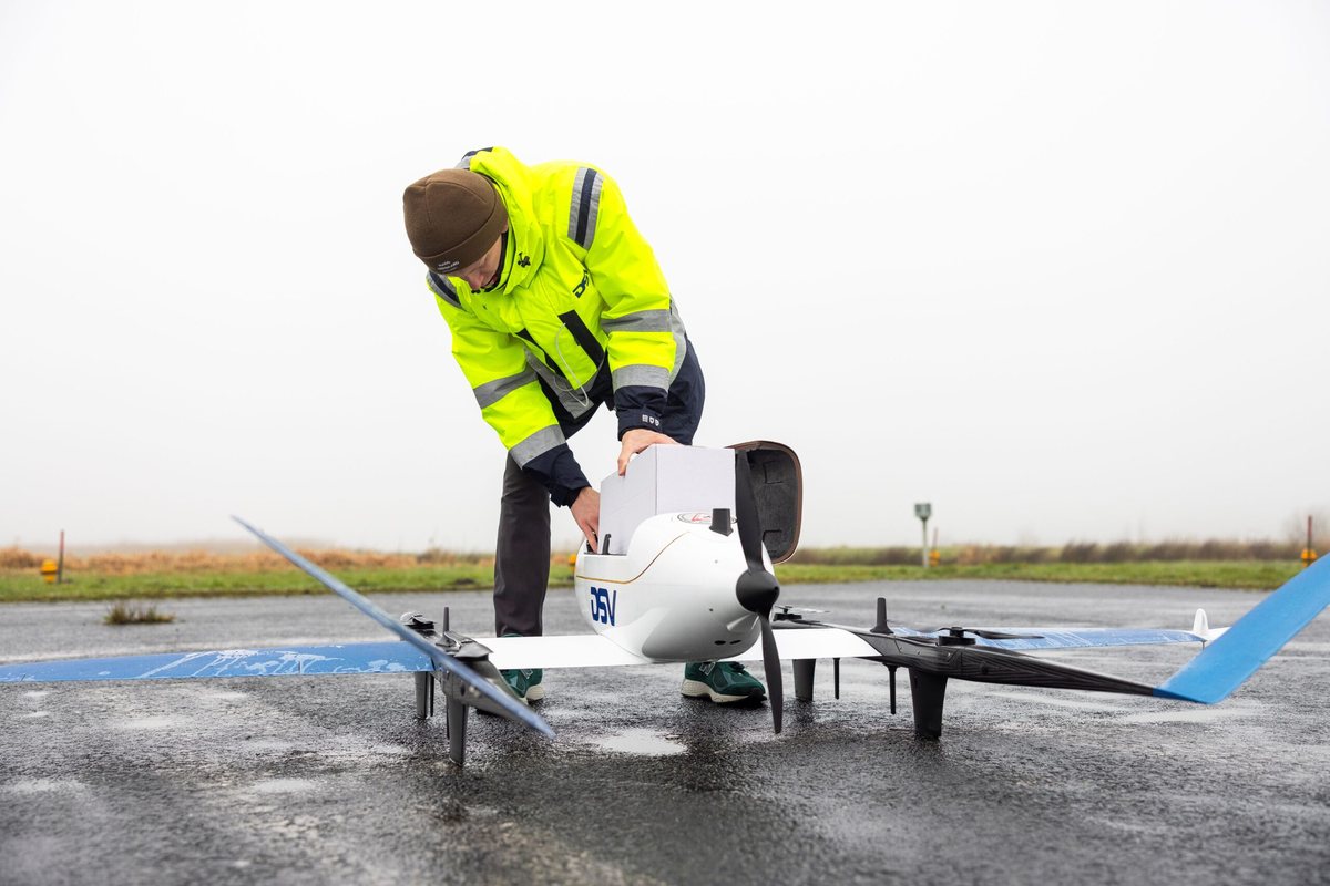 Hvit VTOL-fastvingedrone på bakken ved DSVs anlegg, med personell i DSV-vester ved siden av