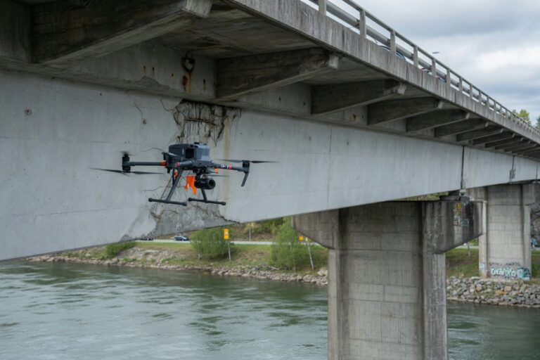 Kvadrokopterdrone svever under en betongbro og inspiserer bjelker og pilarer over vann