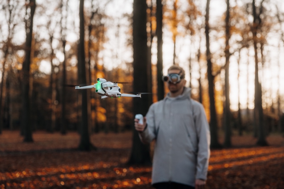 Pilot med Antigravity Vision-briller og håndkontroller styrer en A1-drone mellom trærne i en høstskog