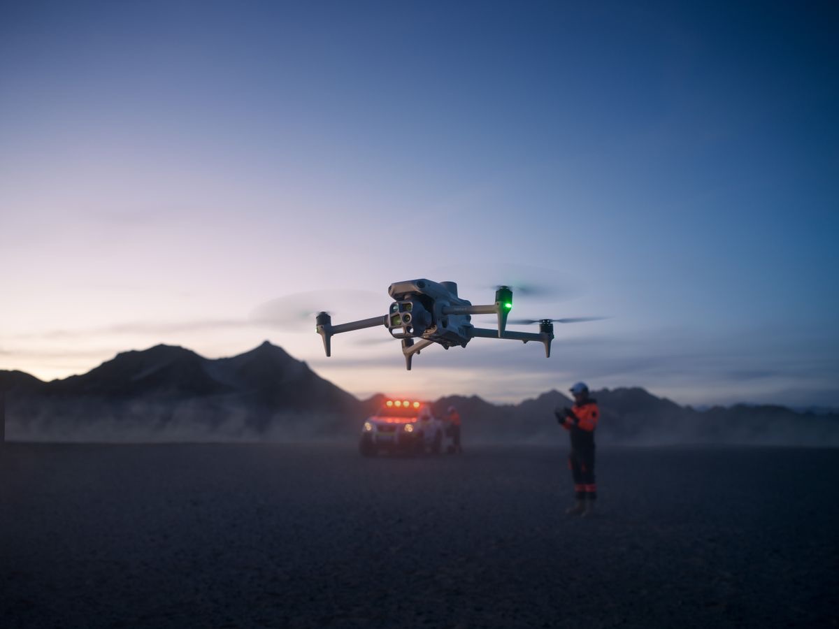 DJI Matrice 4T i lufta i skumringen med et utrykningskjøretøy og en redningsarbeider i bakgrunnen