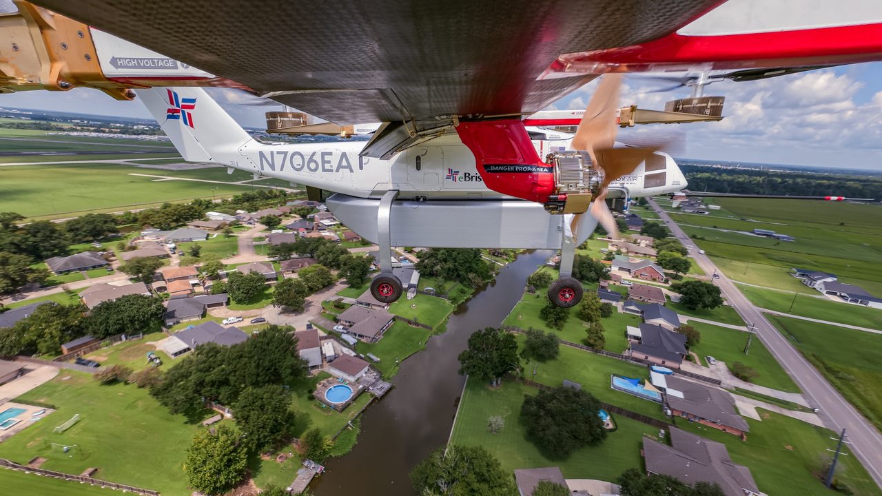 Undersiden av Elroy Air Chaparral i luften med registreringen N706EA, utfelt landingsstell og løfterotorer i gang, over boligfelt og kanaler i Louisiana