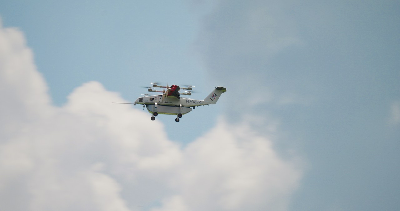 Elroy Air Chaparral i horisontalflukt mot blå himmel med cumulusskyer, med løfterotorer montert på bommer langs skroget