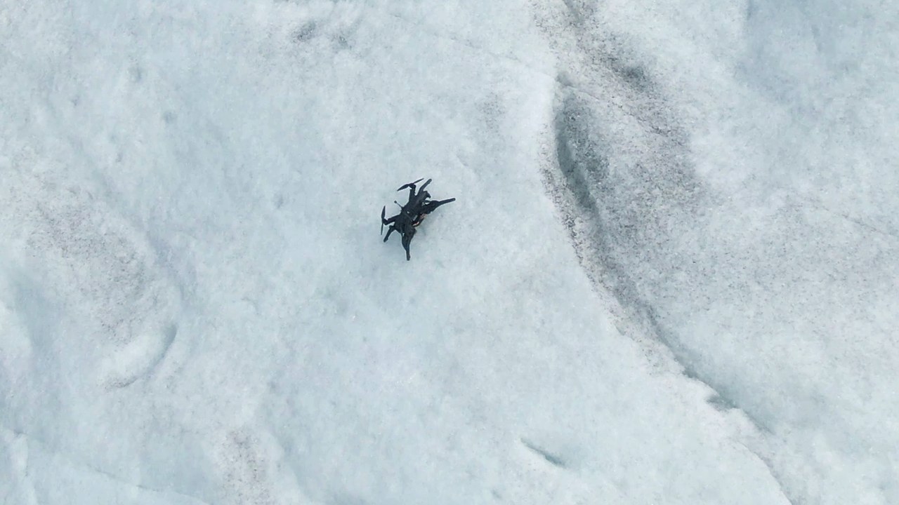 Liten svart drone som står festet på en hvit isbreoverflate, sett ovenfra