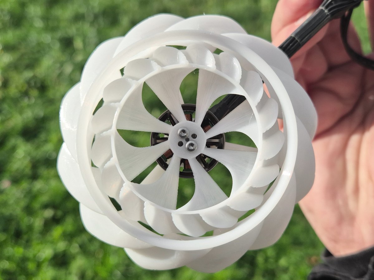 Nærbilde av en hvit 3D-printet radialvifte holdt i hånden, med viftehjulet skrudd rett på en børsteløs motor