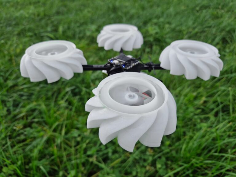 Quadcopter med fire hvite 3D-printede radialvifter i stedet for propeller, fotografert på gresset