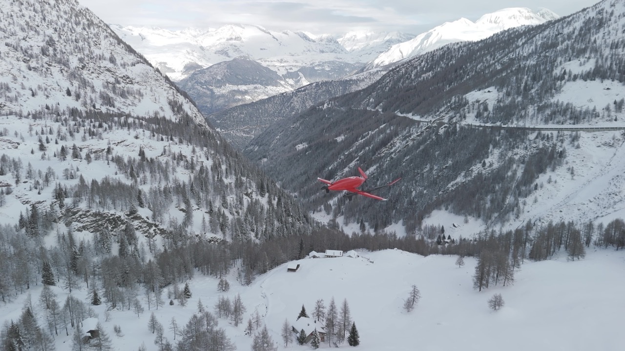 Rød RigiTech Eiger-drone i flukt over en snødekt alpedal med skog og fjell