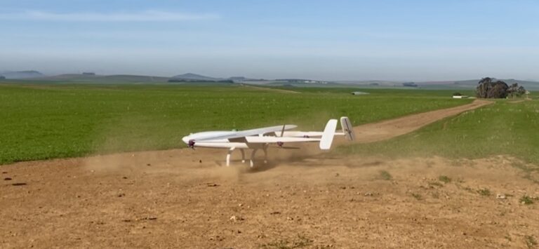 Hvit ShadowfaxUAS SF45 VTOL-drone med fastvinge løfter seg fra en grusvei ved et jorde