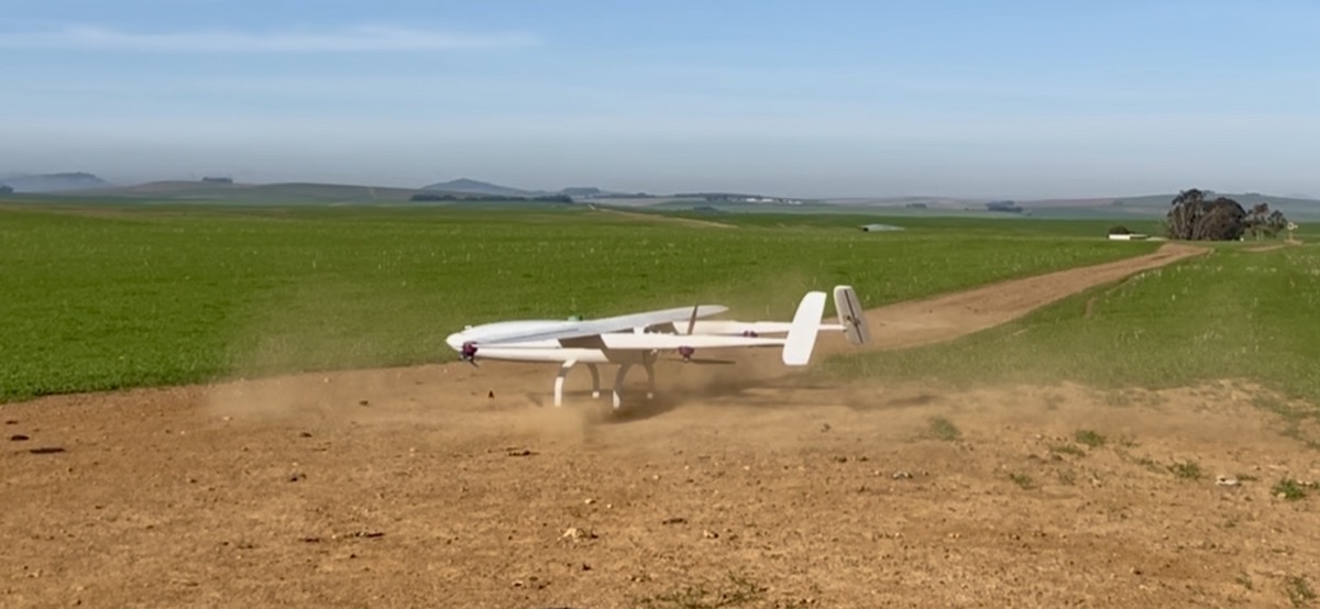 Hvit ShadowfaxUAS SF45 VTOL-drone med fastvinge løfter seg fra en grusvei ved et jorde