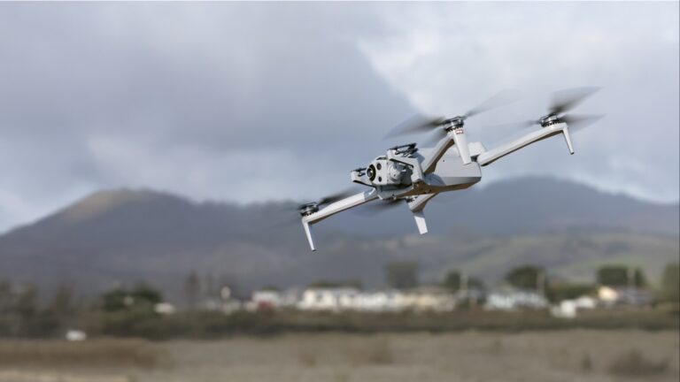 Skydio X10-drone i lufta med fjell og bebyggelse i bakgrunnen
