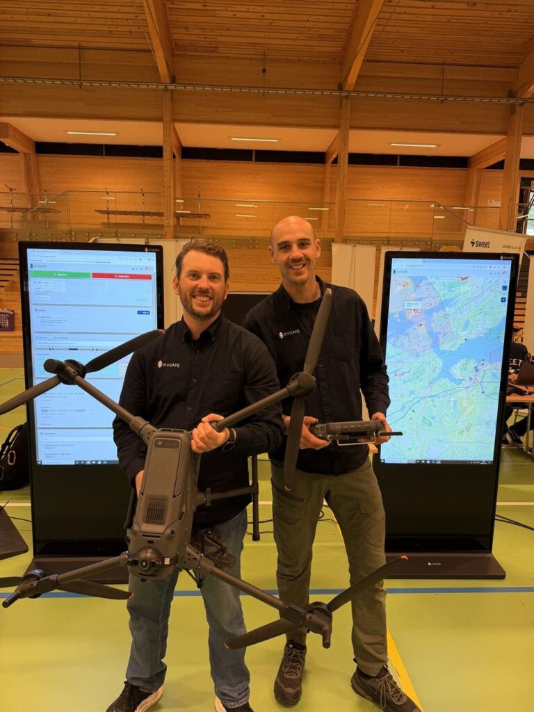 Gard Haug-Hansen holder en drone og Rikard Bjørklund en fjernkontroll foran skjermer med AviSafe