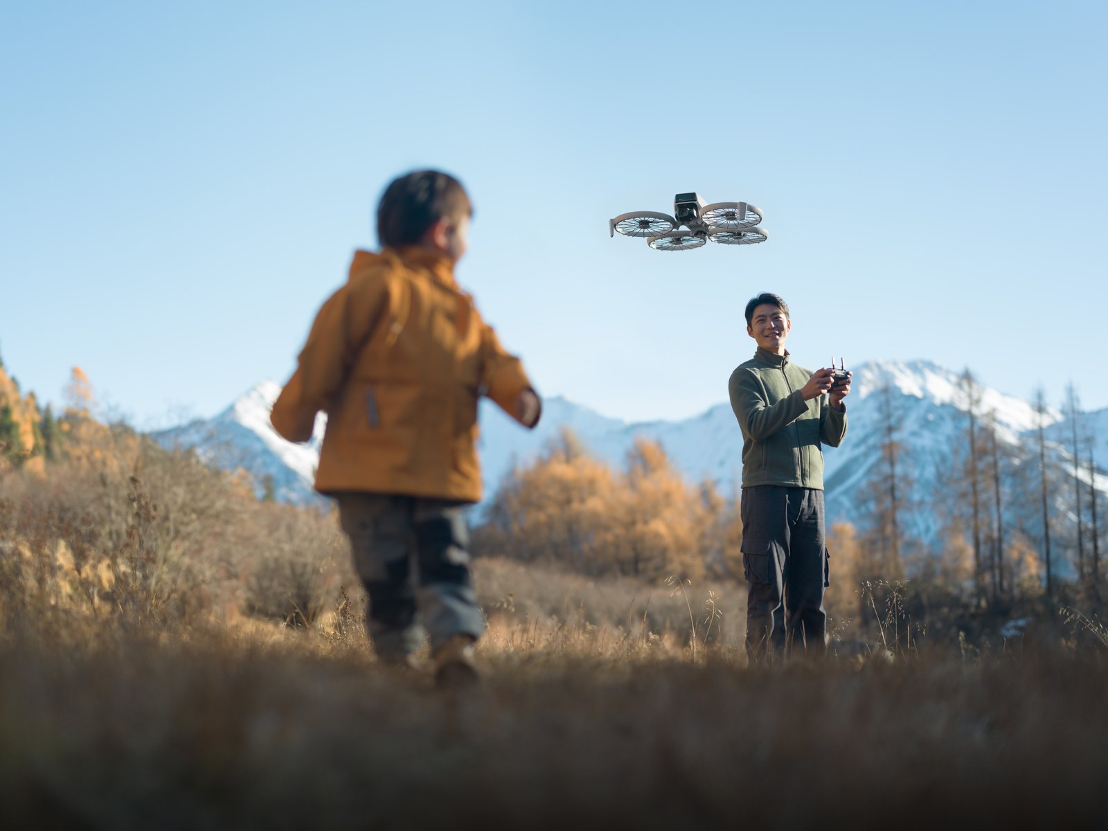 En voksen flyr DJI Flip i fjellet mens et barn går i forgrunnen